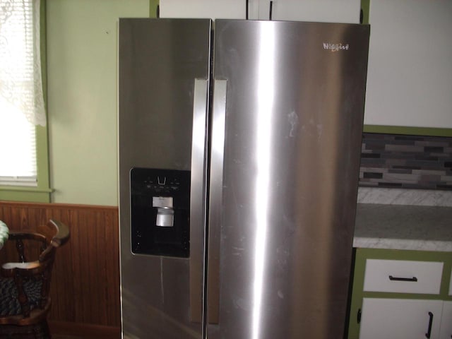 details with white cabinetry, stainless steel fridge, and wooden walls