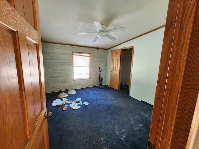 unfurnished bedroom with crown molding, ceiling fan, wood walls, and dark colored carpet