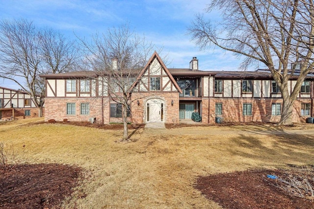 english style home with brick siding, a chimney, and a front yard