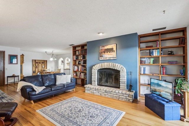 living area with a fireplace, visible vents, a textured ceiling, wood finished floors, and a chandelier