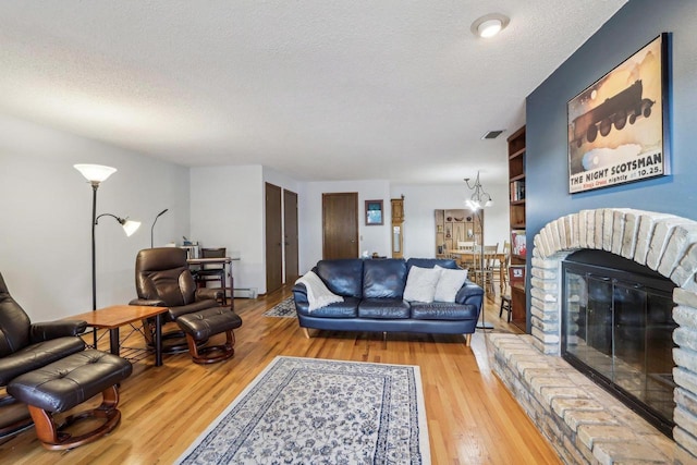 living room featuring a textured ceiling, a fireplace, wood finished floors, and a chandelier