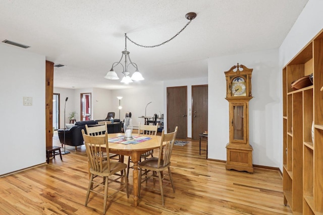 dining space featuring baseboards, visible vents, a chandelier, and wood finished floors