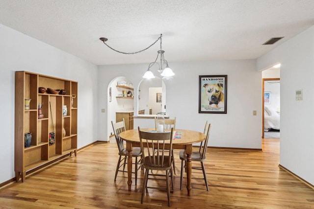 dining room with arched walkways, visible vents, a textured ceiling, and light wood-style flooring