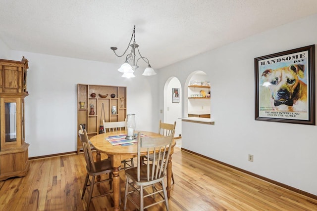 dining room with a chandelier, light wood-style flooring, baseboards, and a textured ceiling