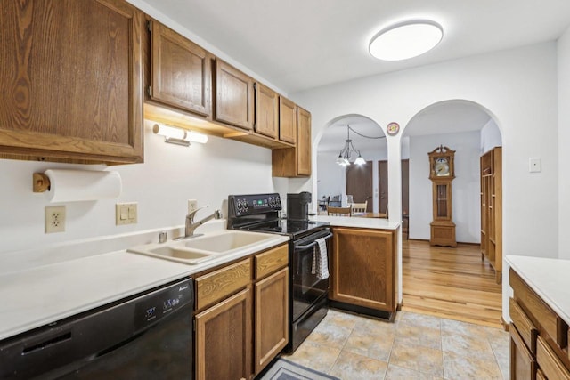 kitchen featuring brown cabinets, decorative light fixtures, light countertops, a sink, and black appliances