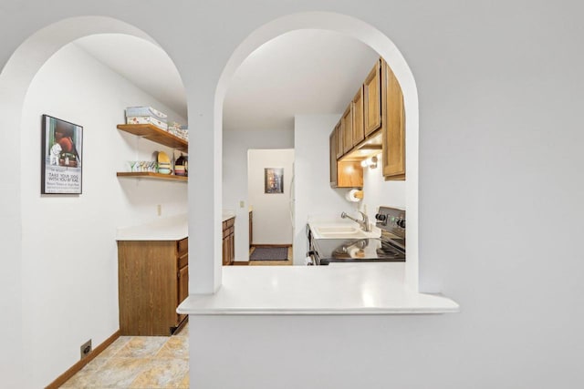 kitchen featuring brown cabinetry, baseboards, light countertops, and stainless steel range with electric cooktop