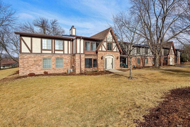 tudor home with a front lawn, a chimney, brick siding, and stucco siding