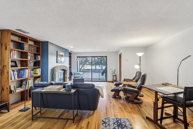 living area with a textured ceiling, a brick fireplace, wood finished floors, and visible vents