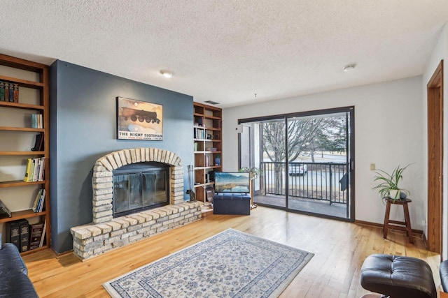 living room featuring baseboards, hardwood / wood-style floors, a textured ceiling, a brick fireplace, and built in shelves