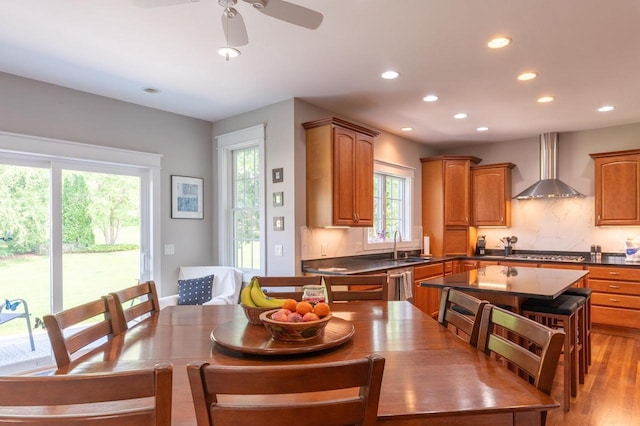 kitchen featuring decorative backsplash, a center island, stainless steel appliances, wall chimney range hood, and light hardwood / wood-style flooring