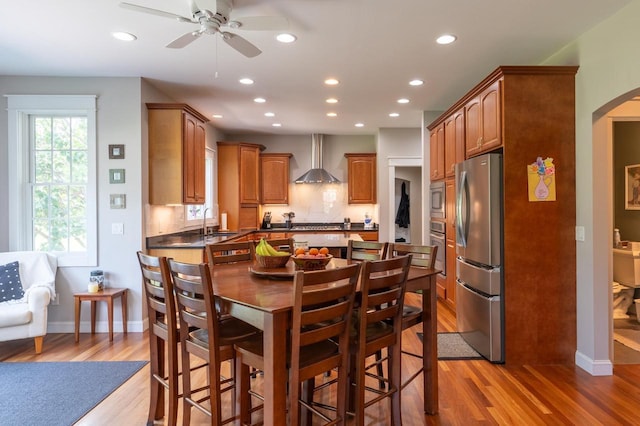 kitchen featuring wall chimney range hood, backsplash, light hardwood / wood-style flooring, and stainless steel appliances