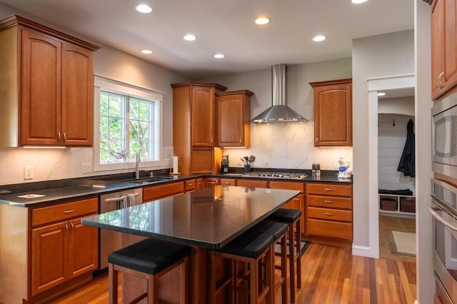 kitchen featuring wall chimney range hood, sink, a breakfast bar, stainless steel appliances, and a kitchen island