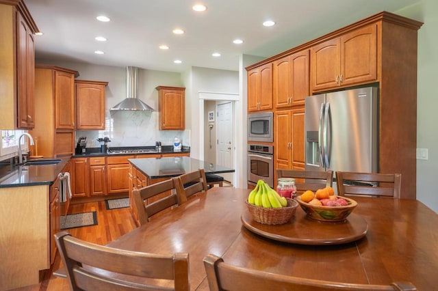 kitchen with tasteful backsplash, sink, stainless steel appliances, light wood-type flooring, and wall chimney exhaust hood