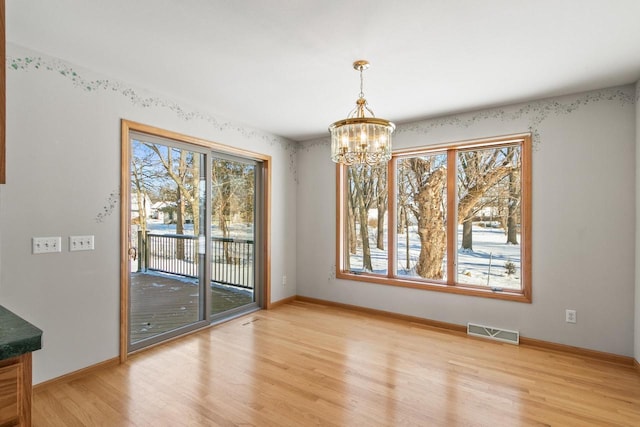 unfurnished dining area with a wealth of natural light, light hardwood / wood-style flooring, and a chandelier