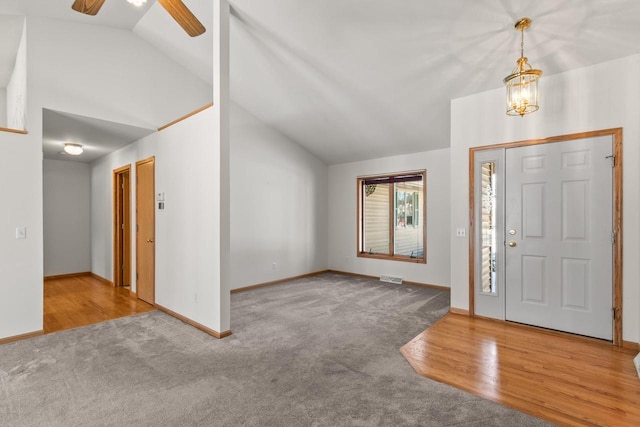 entryway with ceiling fan with notable chandelier, light colored carpet, and high vaulted ceiling