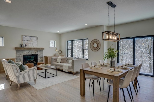 dining space with a stone fireplace, a textured ceiling, and light wood-type flooring