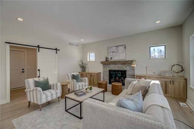 living room featuring a stone fireplace, a barn door, and light wood-type flooring