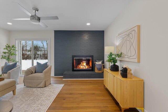 living area with a fireplace, ceiling fan, and light wood-type flooring