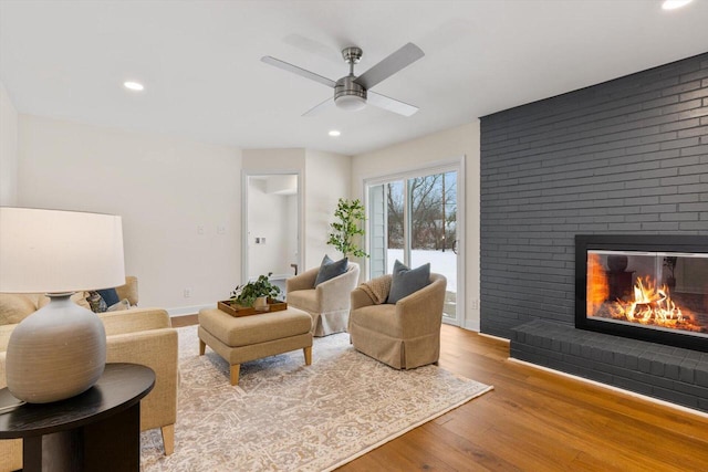 living room featuring ceiling fan, a brick fireplace, and light wood-type flooring