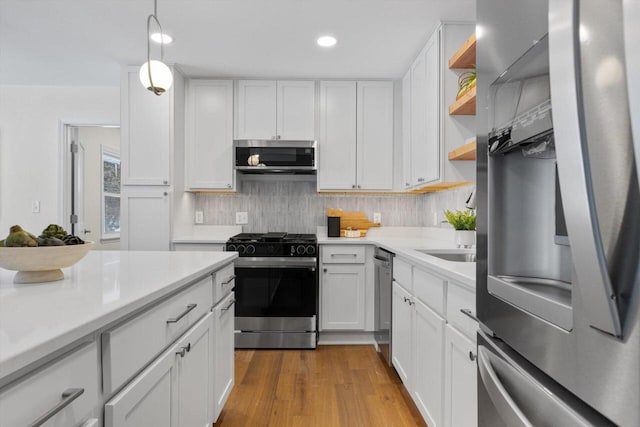 kitchen with appliances with stainless steel finishes, pendant lighting, white cabinets, and backsplash