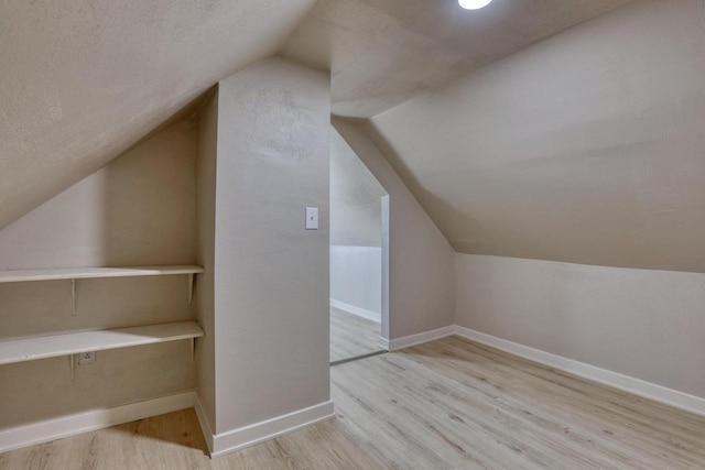 additional living space with baseboards, vaulted ceiling, a textured ceiling, and light wood finished floors