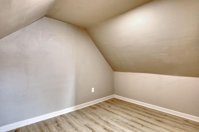 additional living space with baseboards, vaulted ceiling, and light wood-style floors