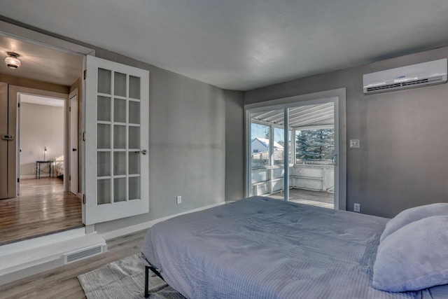 bedroom with access to outside, a wall unit AC, visible vents, and light wood finished floors