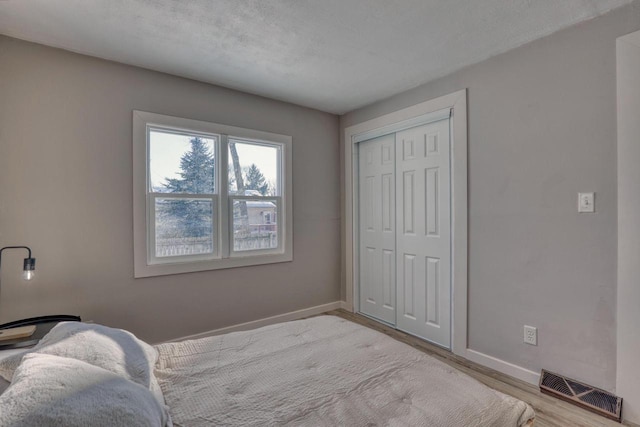 bedroom featuring a closet, light wood-type flooring, visible vents, and baseboards