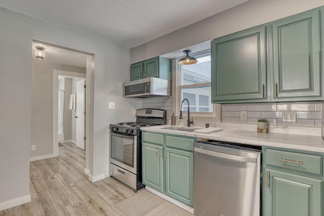 kitchen with stainless steel appliances, tasteful backsplash, light wood-style flooring, a sink, and green cabinetry