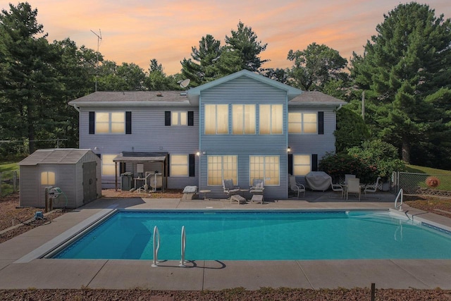 back house at dusk with a storage shed, a patio, and a fenced in pool