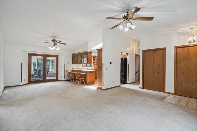 unfurnished living room with ceiling fan with notable chandelier, vaulted ceiling, light carpet, and french doors