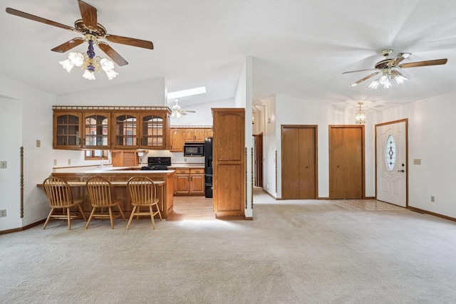 kitchen with lofted ceiling with skylight, a breakfast bar area, light colored carpet, ceiling fan, and kitchen peninsula