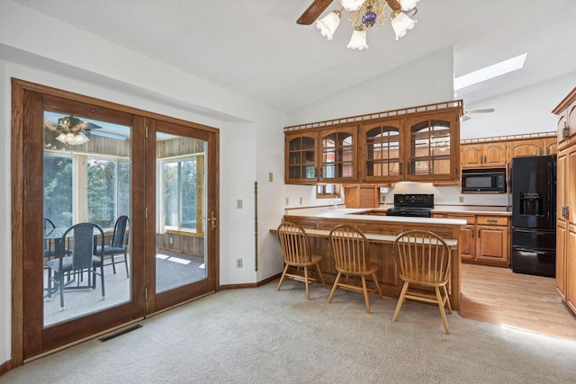 kitchen with vaulted ceiling with skylight, kitchen peninsula, a breakfast bar area, ceiling fan, and black appliances