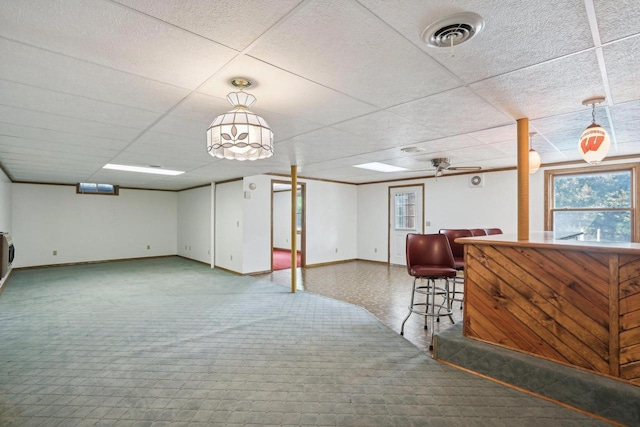 basement featuring ceiling fan, bar area, and a drop ceiling