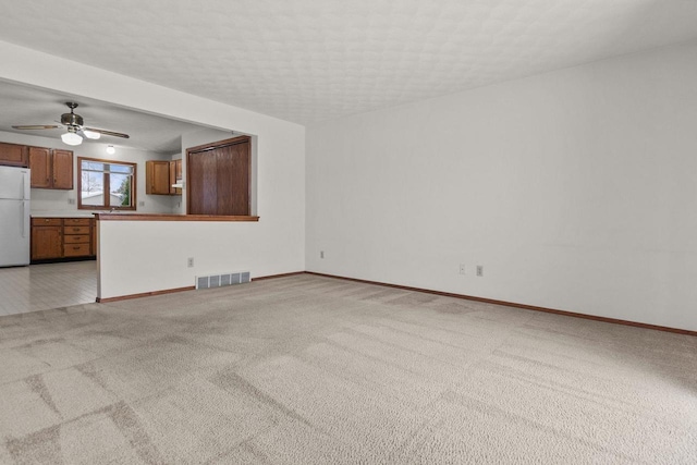 unfurnished living room with ceiling fan, light colored carpet, and a textured ceiling