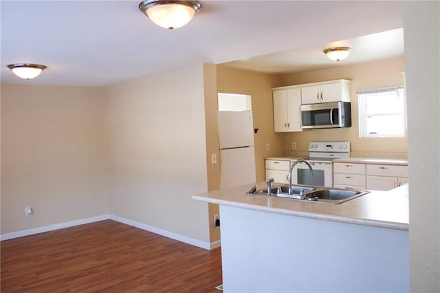 kitchen featuring sink, dark hardwood / wood-style flooring, kitchen peninsula, white appliances, and white cabinets