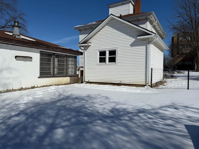 view of snow covered exterior featuring a chimney and fence