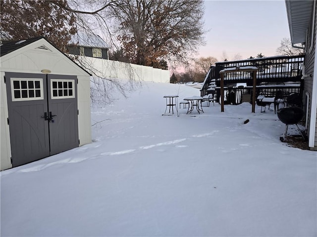 snowy yard featuring fence, a wooden deck, and a storage unit