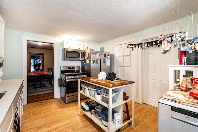 kitchen featuring white cabinetry, appliances with stainless steel finishes, a textured ceiling, and light wood-type flooring