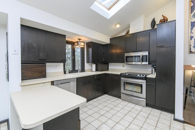 kitchen with vaulted ceiling with skylight, a peninsula, a sink, light countertops, and appliances with stainless steel finishes