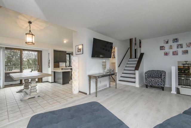 living area with light wood-style flooring, visible vents, stairway, and baseboards