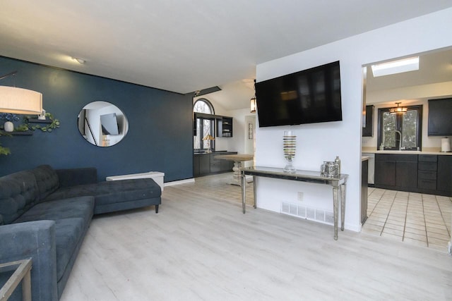 living room featuring light wood-style flooring, visible vents, vaulted ceiling, and baseboards