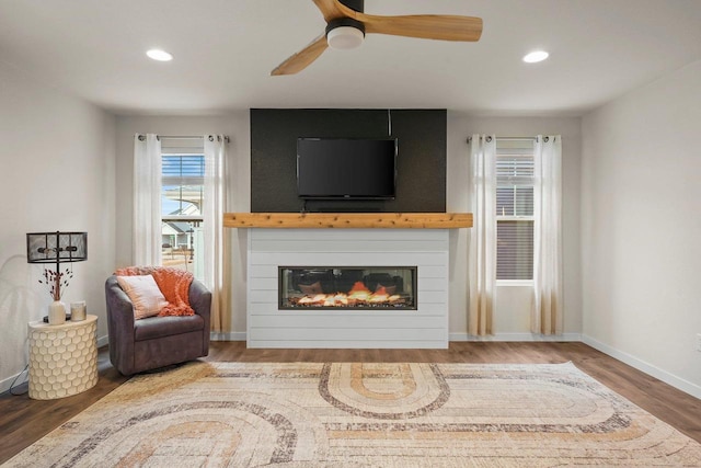 living area with recessed lighting, a glass covered fireplace, ceiling fan, wood finished floors, and baseboards