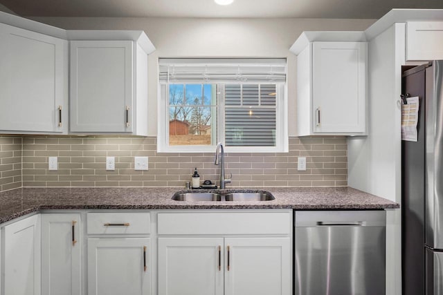 kitchen with backsplash, appliances with stainless steel finishes, white cabinets, a sink, and dark stone countertops