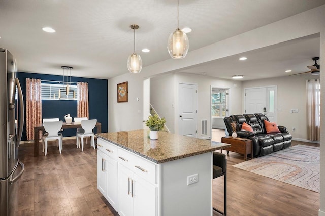 kitchen with wood finished floors, a kitchen island, stainless steel fridge, and a kitchen breakfast bar