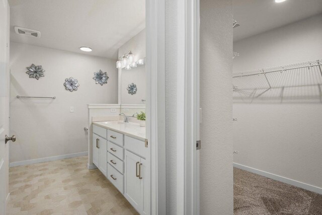 full bath featuring a walk in closet, visible vents, vanity, and baseboards