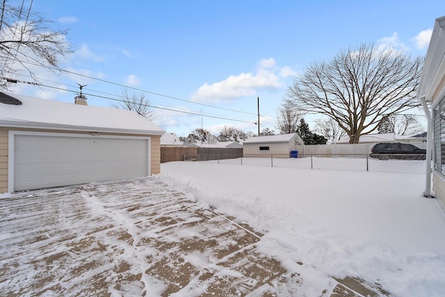 snowy yard with a garage and an outbuilding