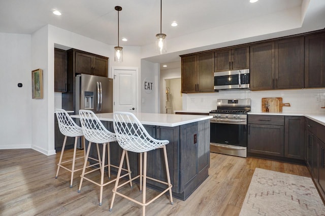 kitchen with stainless steel appliances, light countertops, hanging light fixtures, and a kitchen island