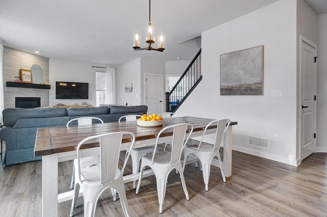 dining area with a large fireplace, visible vents, wood finished floors, stairs, and a chandelier