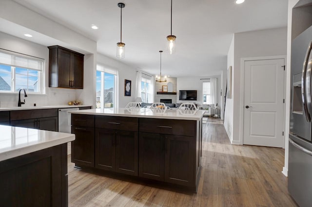 kitchen featuring light countertops, open floor plan, dark brown cabinetry, a sink, and stainless steel fridge